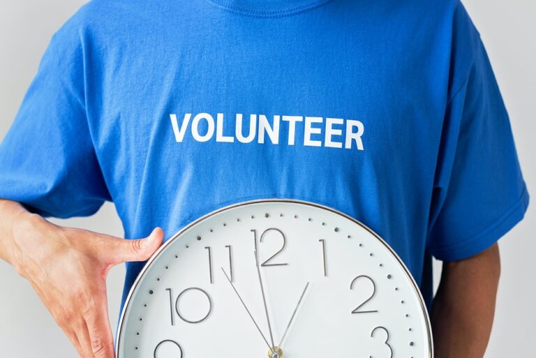 Volunteer in blue tshirt with 'volunteer' on holds a clock signifying time. Photo: Pexels
