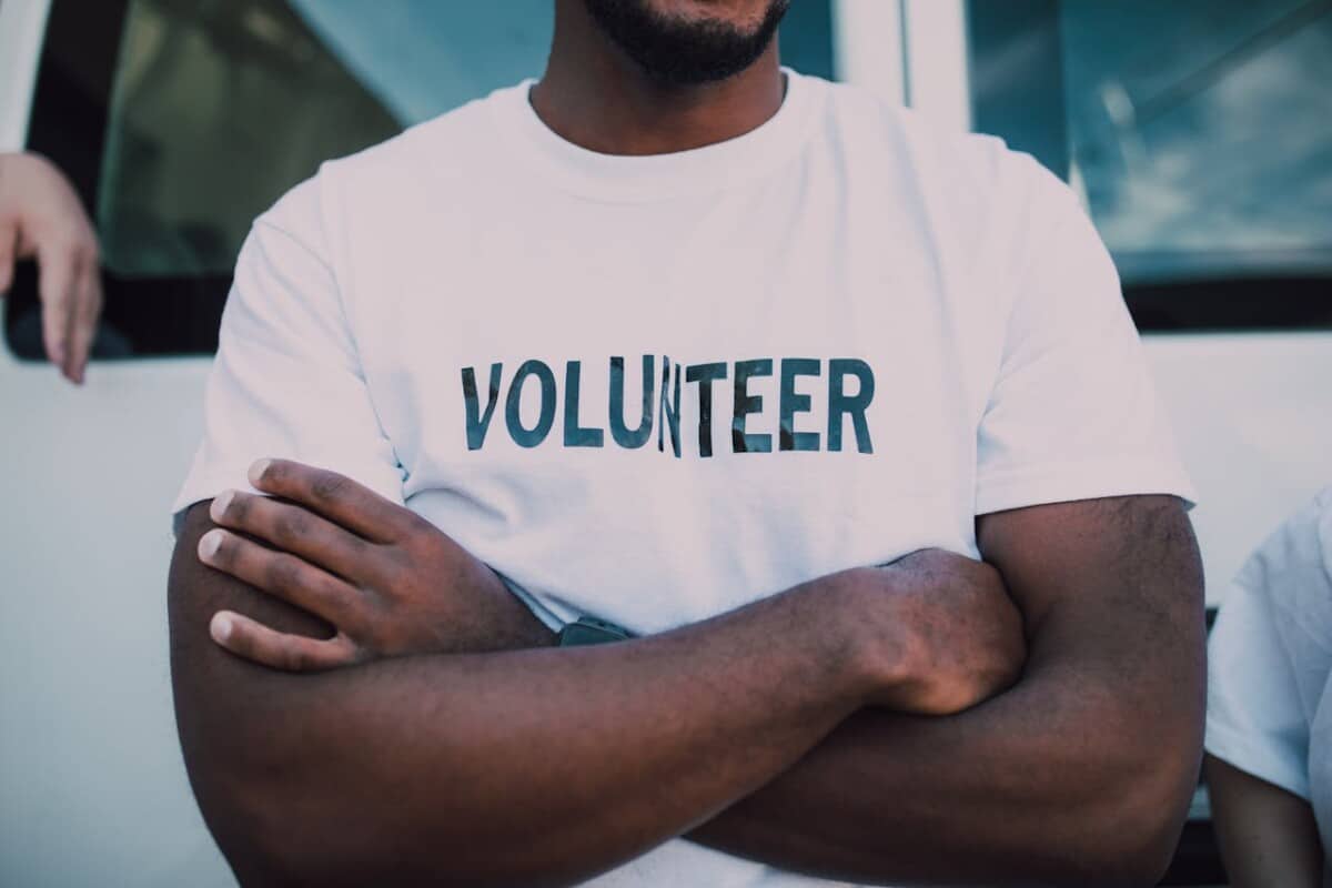 Volunteer, standing with folded arms, wearing a white tshirt with 'volunteer' in capitals on the front.