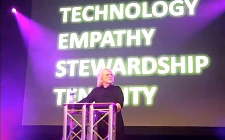 Kay Sprinkel Grace at a lectern at IFC in front of a screen with the words 'technology, empathy, stewardship and tenacity' in capitals