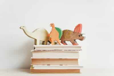 Wooden toy dinosaurs on top of a pile of books.