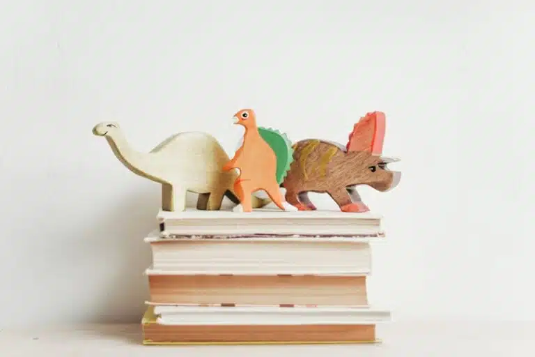 Wooden toy dinosaurs on top of a pile of books.