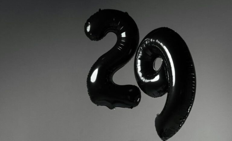 Two balloons, one shaped as a number two, the other as a nine, making 29. Black and white image.