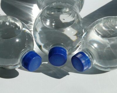 Three transparent plastic bottles of water, each with a blue screw top, resting on their sides on a white table top.
