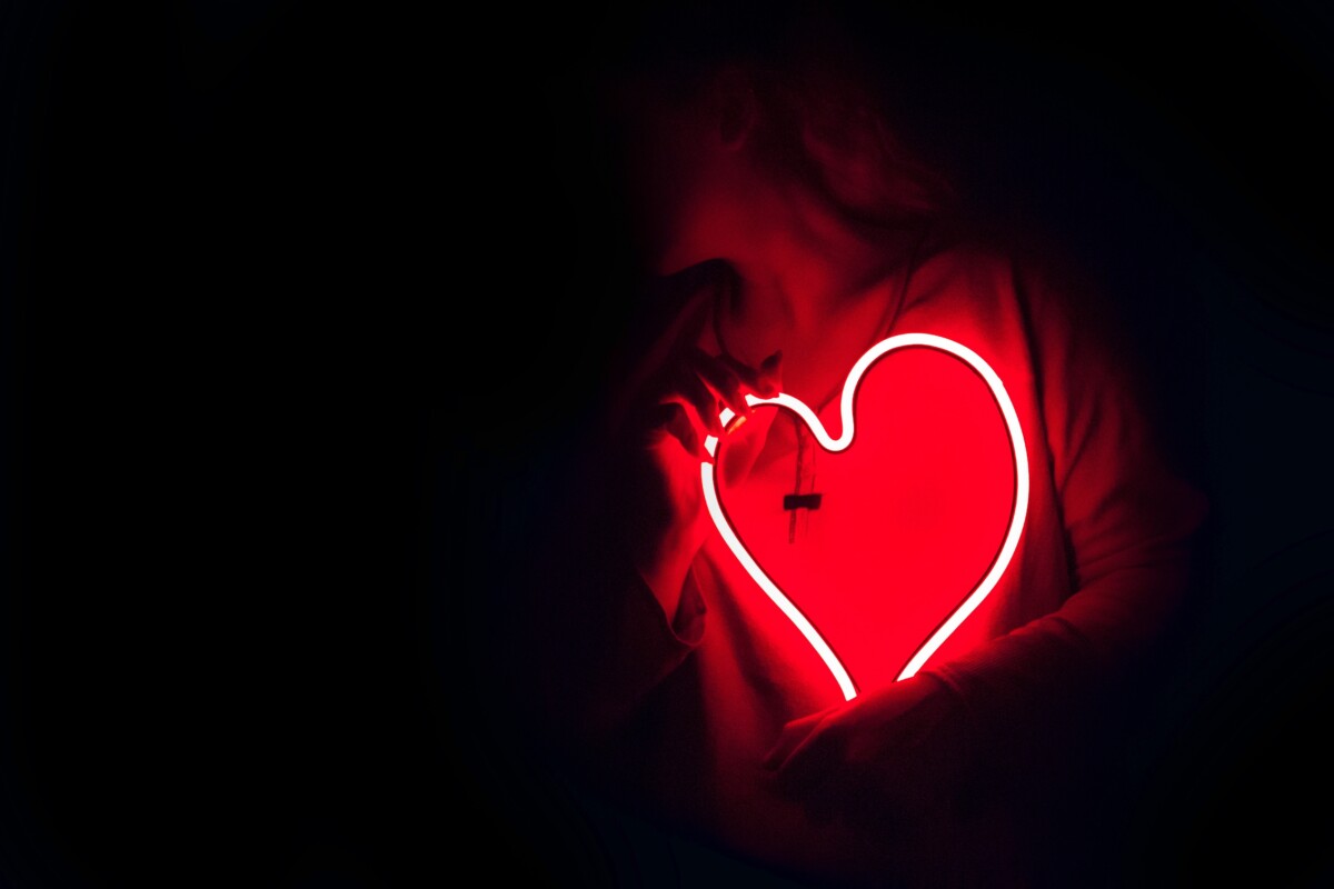 Red neon heart shape held by woman in a dark room. Photo: Pexels.com