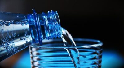 Water being poured from a bottle into a glass, against a blue background.