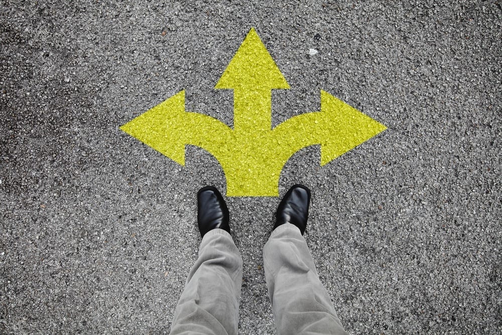 Looking down at two feet with three different arrows painted on ground indicating a choice of direction