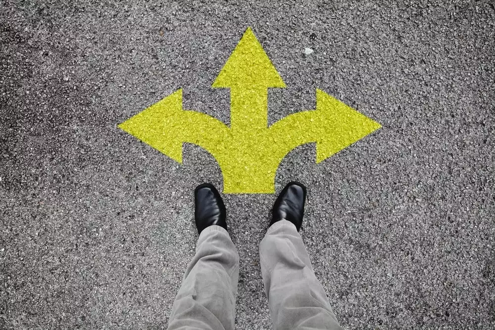 Looking down at two feet with three different arrows painted on ground indicating a choice of direction