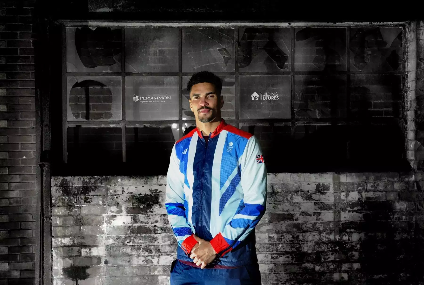 Anthony Ogogo stands against a wall with logos of Persimmon Homes and Building Futures