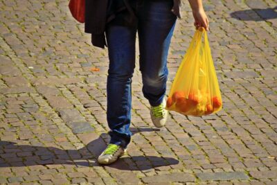 Yellow plastic bag holding tomatoes is carried across a cobbled road. Photo: Pixabay