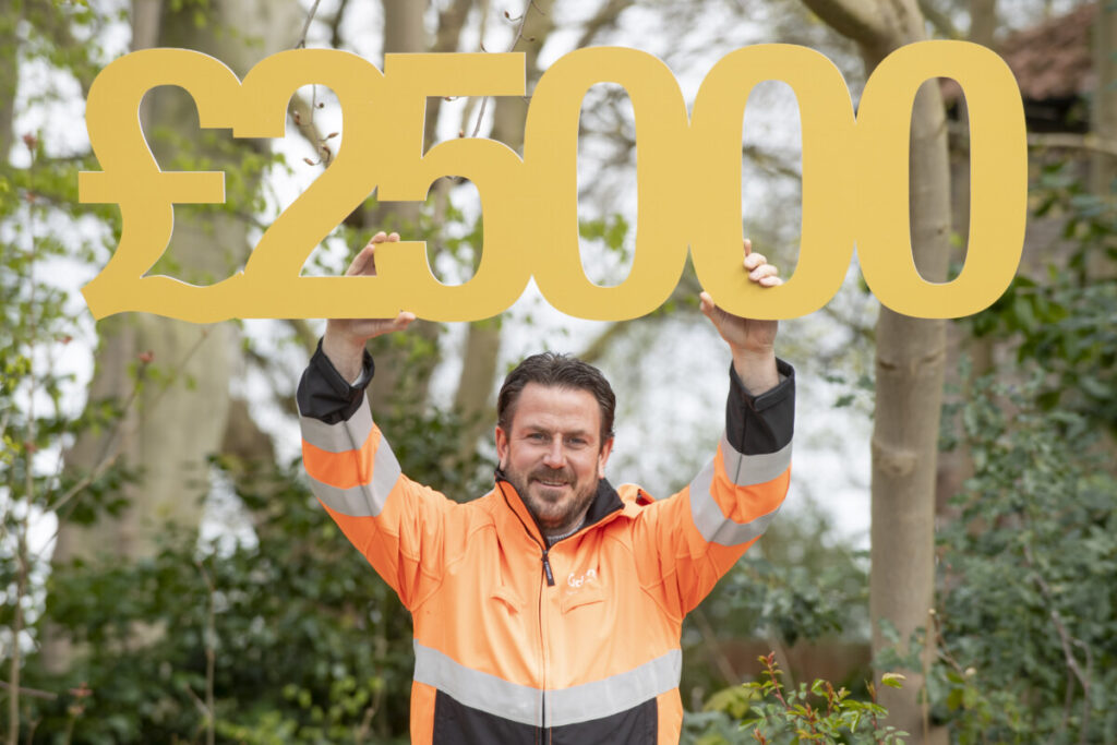 A man in a hi-vis jacket holding up a cut-out of the figure of £25,000