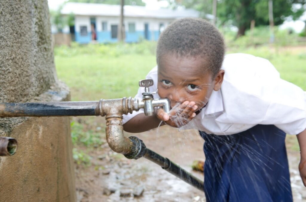 A child in Tanzania drinking from a water tap from charity EDUKaid