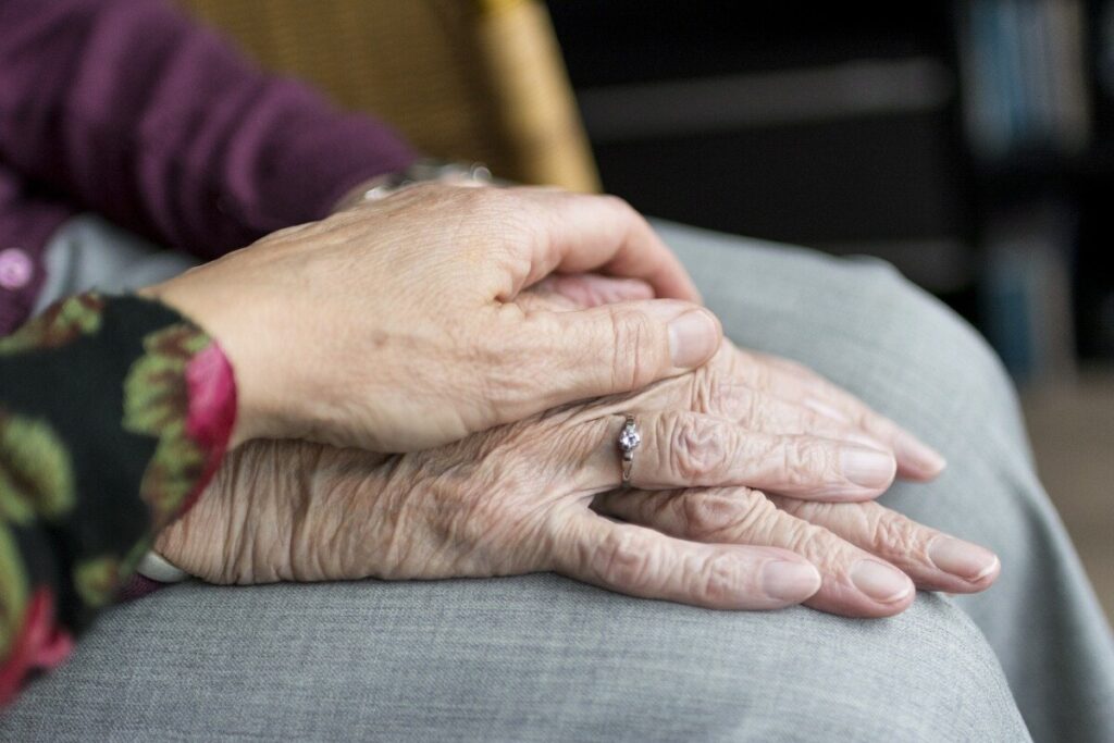 The hand of a middle aged woman lies on top of an elderly woman's hands
