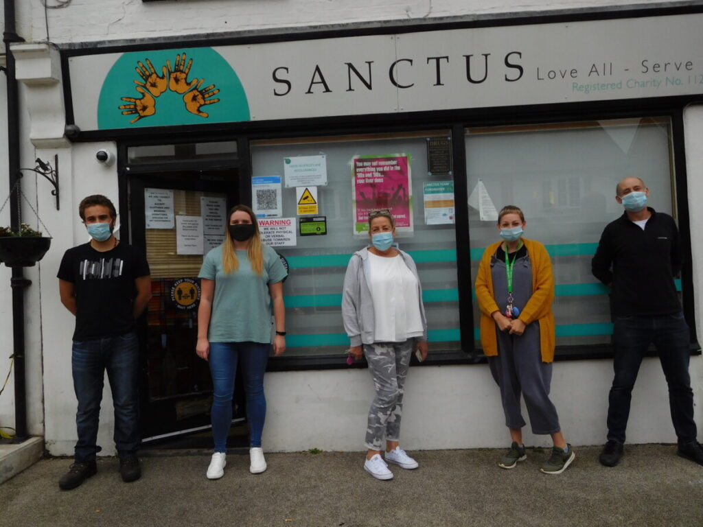 People from the charity Sanctus standing outside their office window, wearing masks