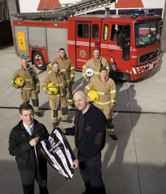 Signed Newcastle FC shirt held by a group of firefighters in front of their fire engine