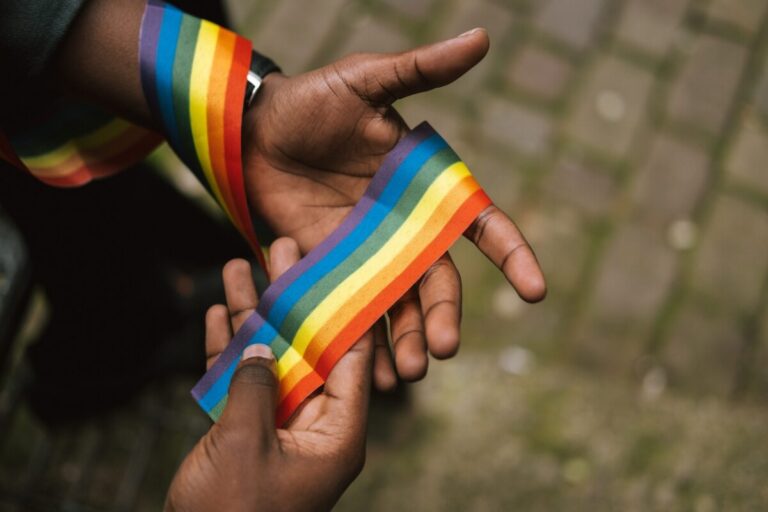 Black man's hands holding a rainbow ribbon - photo: Pexels
