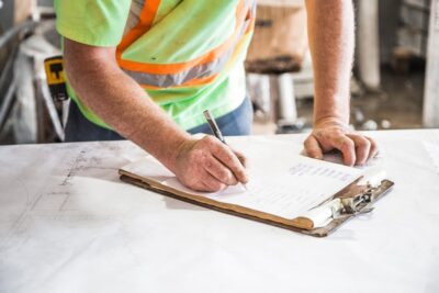 Man in hi-viz jacket signs paper on a clipboard with a pen. Photo: Pexels.com