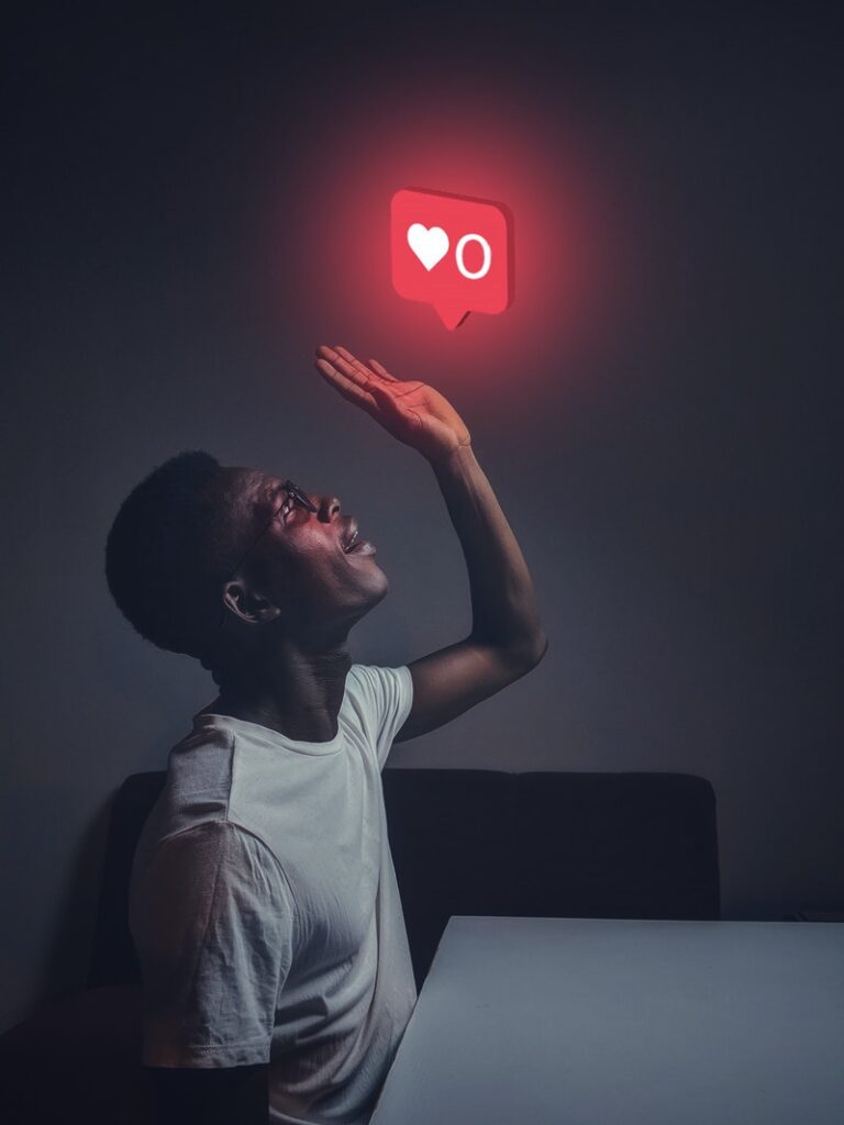 Man at table raising his hand to a glowing zero likes/hearts social media icon. Photo: Pexels