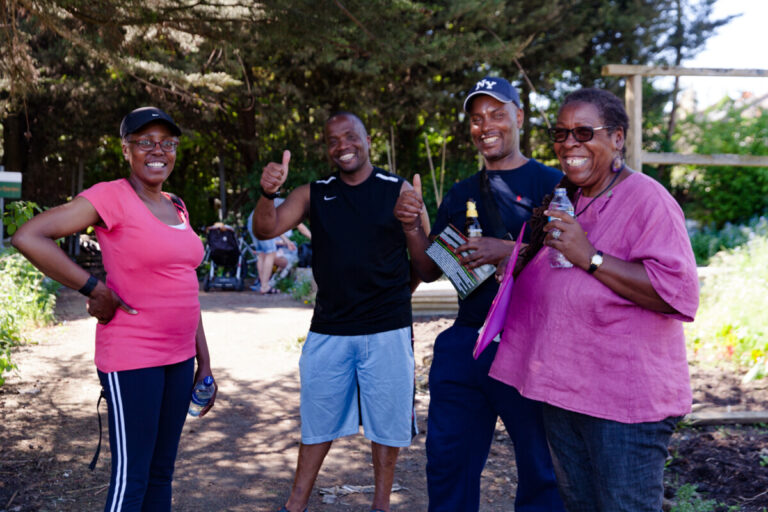 Group of Black middle-aged adults mainly in workout clothing in a park smiling at the camera