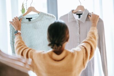 A woman holding up a jumper and a shirt on hangers