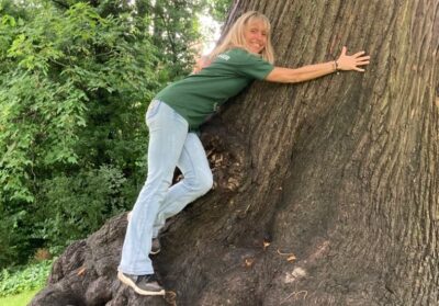 Michaela Strachan in green t-shirt & light blue jean hugging a very big trees