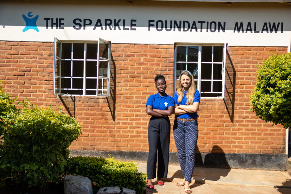 two young women from the Sparkle Foundation outside a red brick building