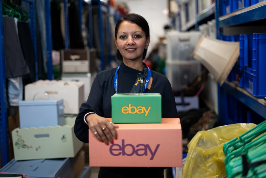 eBay for Charity - woman holding boxes marked eBay for Charity in warehouse of shelves. Vision International