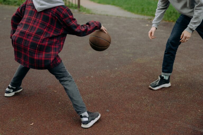 Two boys playing basketball in jeans & trainers