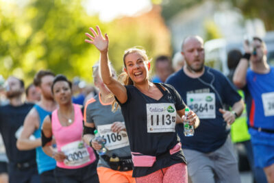 A woman runner smiles and raises her hand in the Ealing Half Marathon. Photo: George Blonsky