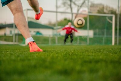 a man in orange boots kicks a football towards the net