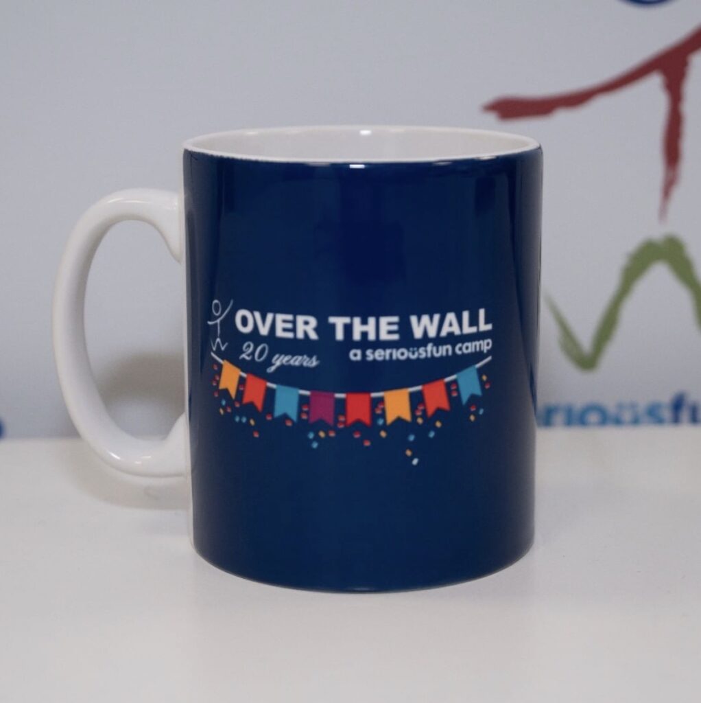 Blue mug on table, with 'Over The Wall. A serious fun camp' text on it, with a row of flags or bunting. Marking the charity's 20th anniversary.

. Photo: Over The Wall
