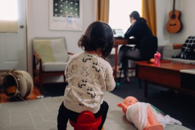 Working from home - a young child plays while their parent/carer works at a desk in their living room. Photo: Unsplash