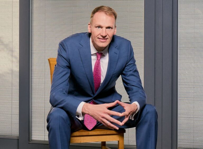 David Knott, the new CEO of the National Lottery Community Fund sits on a chair in a blue suit and pink tie