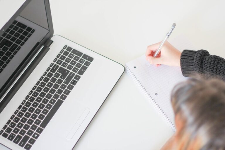 Looking down on a woman writing notes on a notepad, next to a macbook