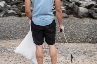 The back of a man in black shorts and blue t-shirt who is litter picking on a beach