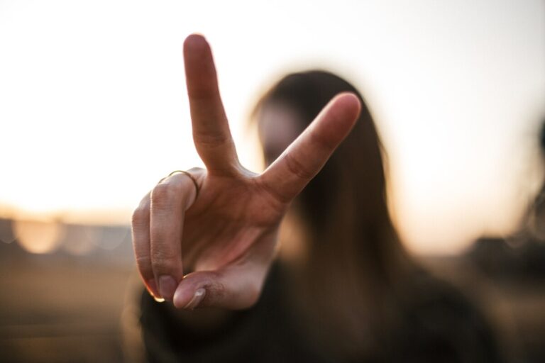 Woman (blurred in background) holding up two fingers suggesting victory or double. Photo: Unsplash