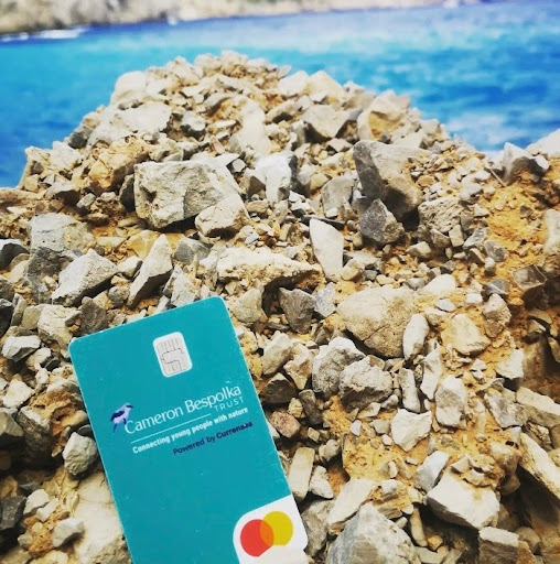 A turquoise currensea debit card on rocks by a blue ocean