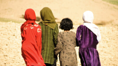 Afghan evacuees - four Afghan girls, photographed from behind, against a dry, stony landscape. Photo: via Allchurches Trust