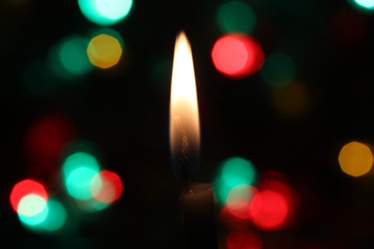 A candle flame against green and red lights on a dark background
