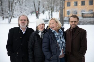 The four members of Abba stand smiling in winter coats against a snowy landscape