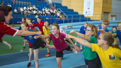 A group of children exercise in a hall wearing brightly coloured gym kit