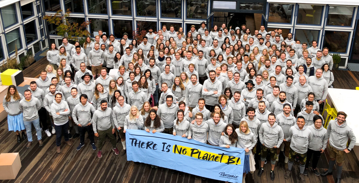 A crowd of people in light grey tops pose with a sign saying 'there is no planet b'