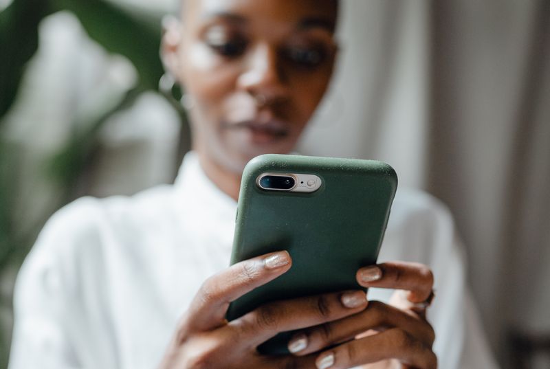 A short haired black woman in a white shirt looks at her phone