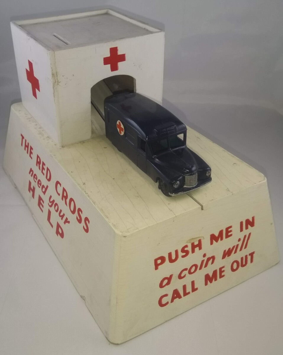 British Red Cross collecting box made from wood. Drop a coin into the garage and the model ambulance springs out. "Push me in - a coin will call me out". Photo: British Red Cross