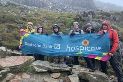 deutsche-bank-employees hold up a hospice uk banner on a rainy rocky hillside