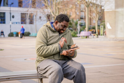A man sits on a bench, smiling during a video call on his tablet