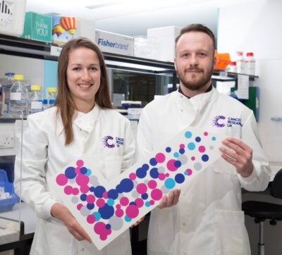 Two research scientists with a large coloured Cancer Research UK tick indicating opt-in