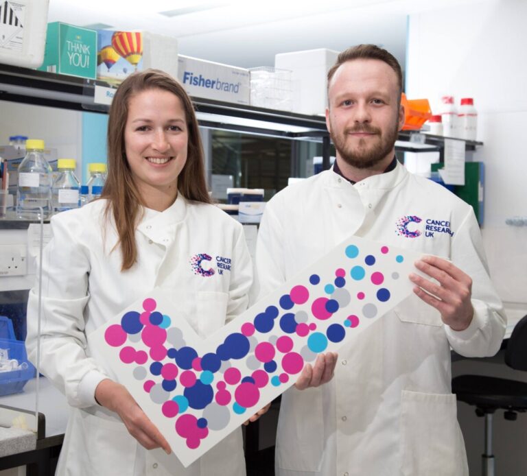 Two research scientists with a large coloured Cancer Research UK tick indicating opt-in