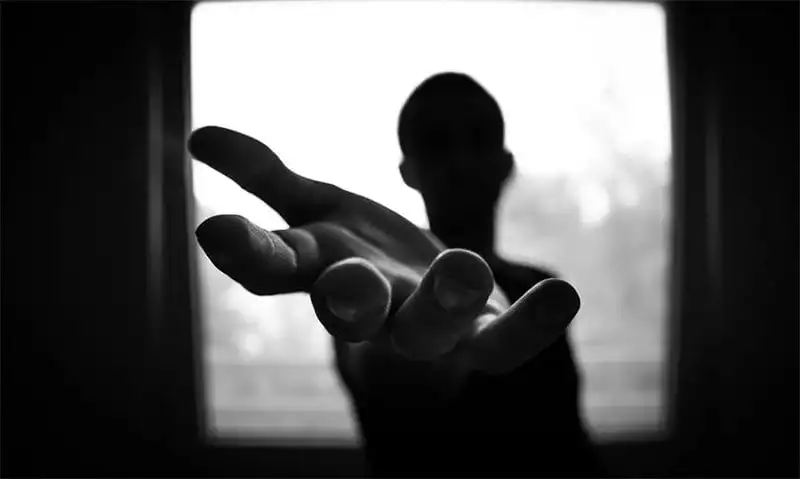 Hand reaches out in the foreground by a person in front of a window. B/W image. Photo: Pexels.com