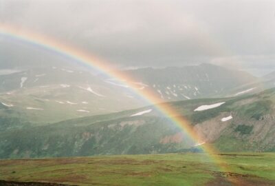 a rainbow over hills with patches of snow on them