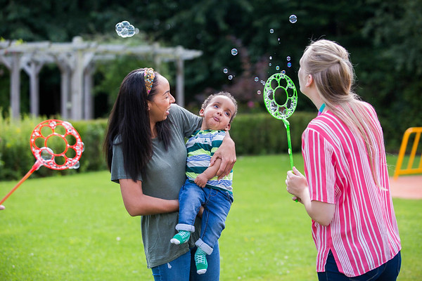a young boy in his mother's arms watches bubbles being blown in a garden